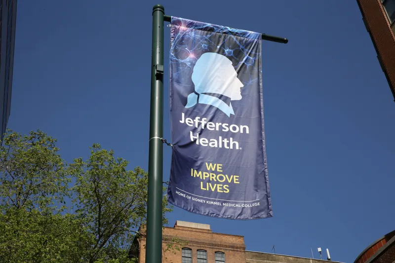 A flag for Jefferson Health hangs off a street post.