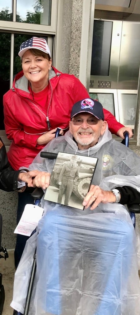 Janet Hewson and her late father, Frederick Huson - US Army, Korean War Veteran, during an Honor Flight they took together. Frederick is holding a picture of his younger self serving in the US Army, while based in Germany. 