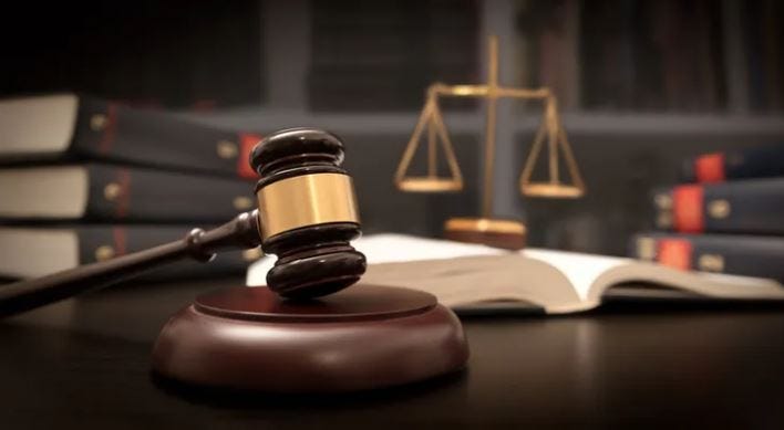 A gavel on a judge's desk. In the background, law books and a set of scales can be seen.