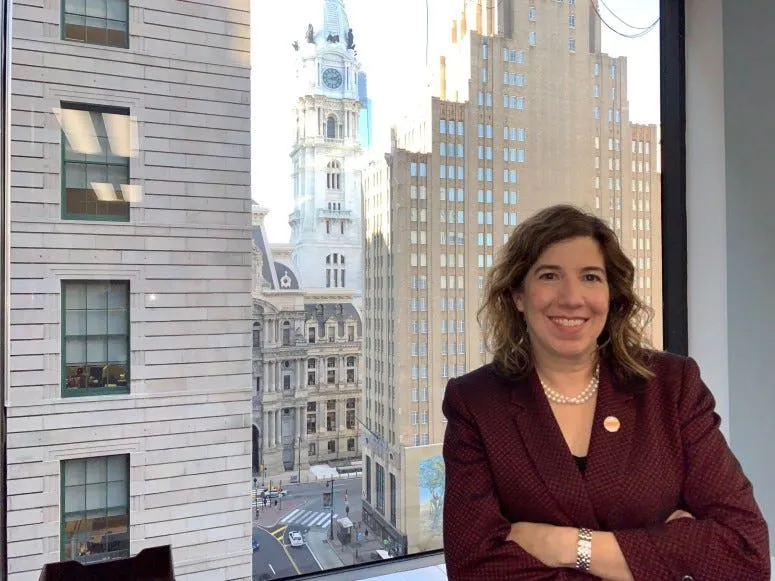 Leslie Richards poses in front of a window with Philadelphia City Hall in the background.