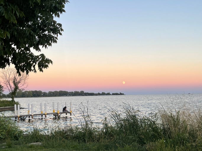 A woman sits on a deck out in Lake St. Clair as the sun sets