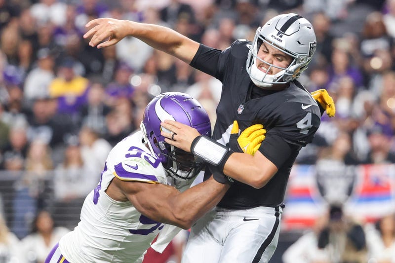 Las Vegas Raiders' QB Aidan O'Connell takes a hit while throwing a pass against the Minnesota Vikings.