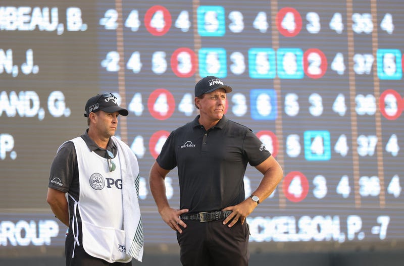 Phil Mickelson and caddie Tim Mickelson stand on the 18th green during the third round of the 2021 PGA Championship, 5/22/21