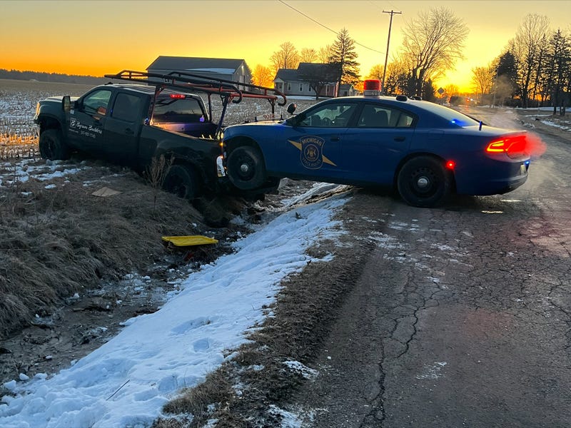 Truck in ditch with MSP patrol car hanging over as sun rises