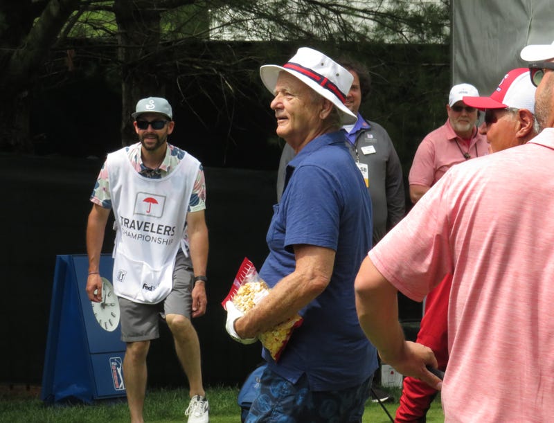 Actor Bill Murray prepares to playfully toss a bag of kettle corn to fans at the Travelers Pro-Am, 6/21/23 in Cromwell