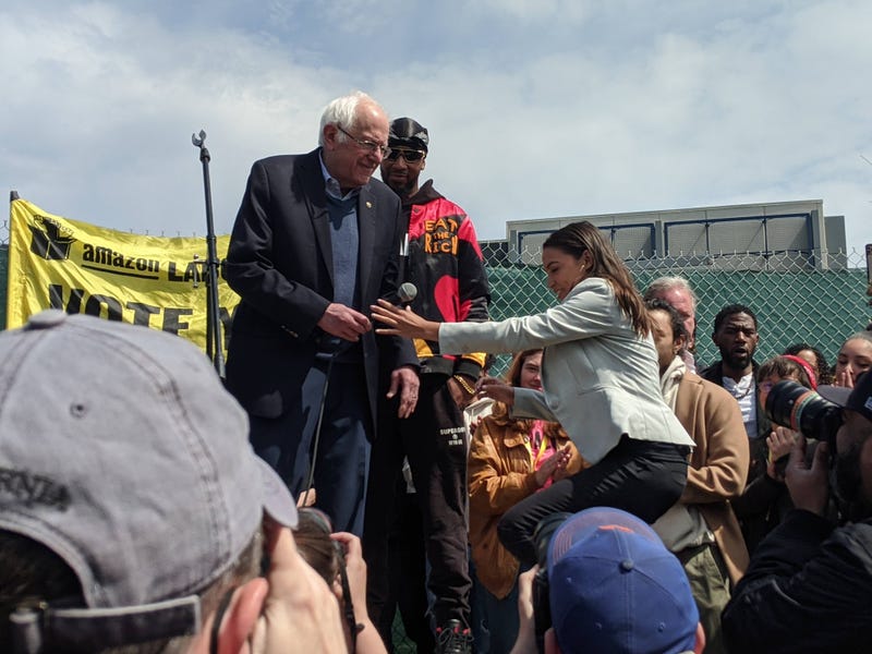 Sanders helps Ocasio-Cortez to the stage with Smalls standing behind him.