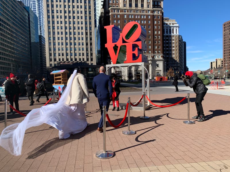 Mike Snader and Amy Brown walk towards Philadelphia Mayor Cherelle Parker, who officiated their wedding in LOVE Park.