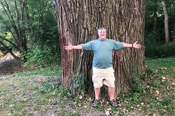 Man poses in front of massive tree in Monroe County