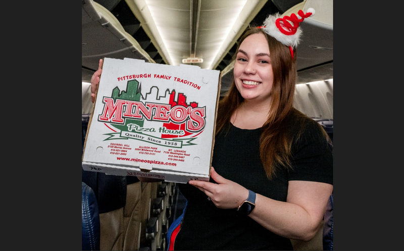 Woman holding a box of Mineo's pizza inside an airplane