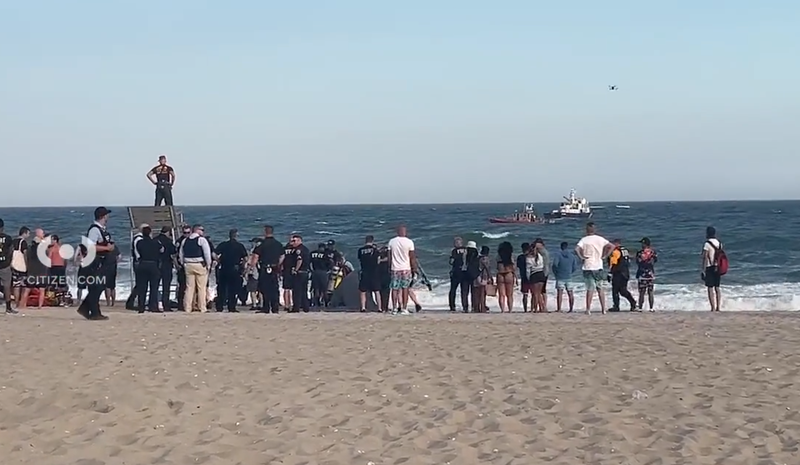 Police and beachgoers observe official sea vessels searching for two missing teen swimmers on Friday night at Jacob Riis Park in Queens.