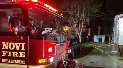 The front of a Novi Fire Department fire truck in front of a row of burned mobile homes. A hose and debris can be seen on the ground.