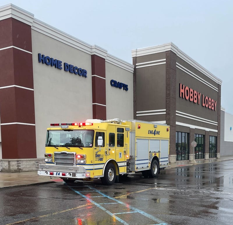 A yellow fire truck is parked near the curb of a Hobby Lobby