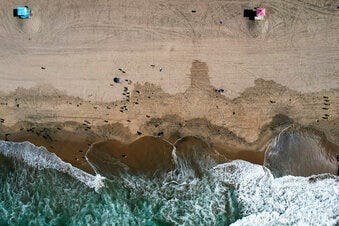 FILE - This Monday, Oct. 11, 2021, aerial file photo taken with a drone, shows beachgoers as workers in protective suits continue to clean the contaminated beach in Huntington Beach, Calif. The amount of crude oil spilled in an offshore pipeline leak in Southern California is believed to be close to about 25,000 gallons, a Coast Guard official said Thursday Oct. 14, 2021.