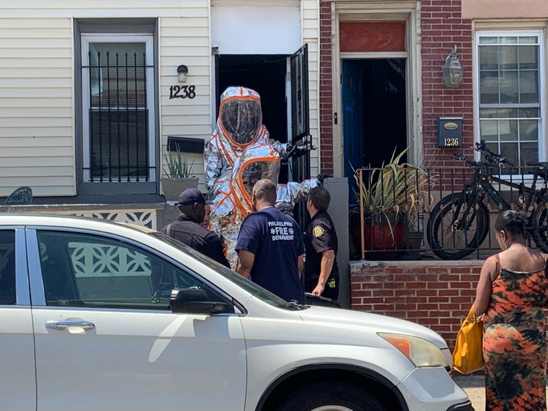 Hazmat crews gather on the stoop of a house neighboring one where the strong odor was first reported.