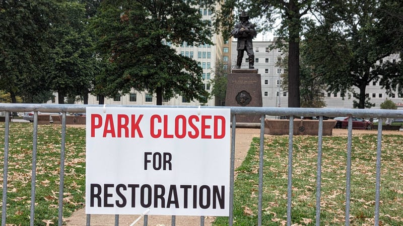The city of St. Louis removes homeless encampment outside city hall. Now a metal barricade encompasses the grass to keep the homeless out. Signs say, "Park closed for restoration."