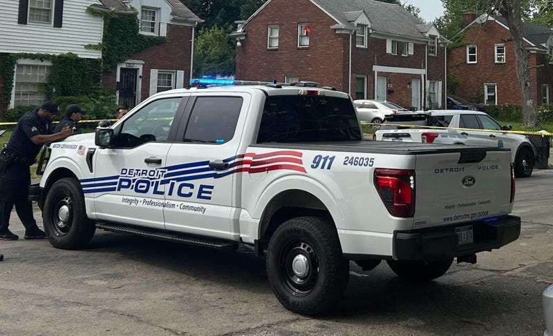 A Detroit Police officer leans on the hood of a police truck; facing the left