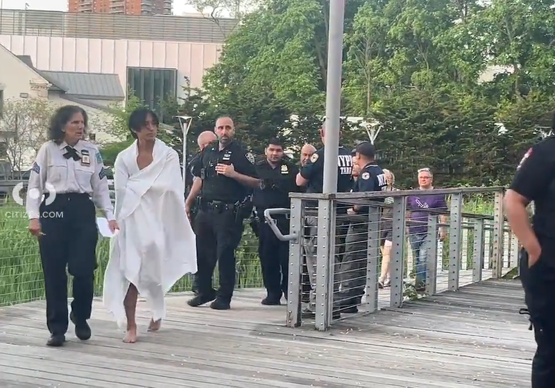 A teen wrapped in a towel walks from the park with first responders