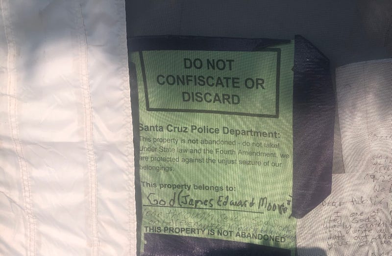 A sign is posted on a tent near the intersection of Highway 1 and Highway 9 in Santa Cruz.