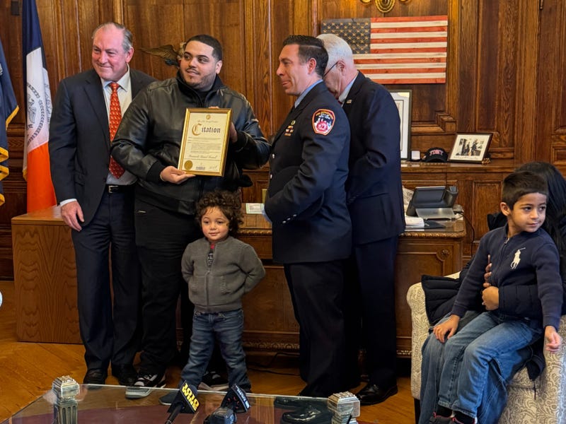 Ian Pereles, 3, poses with officials and his family at a ceremony honoring the firefighters and paramedics who saved him from a fire last month.