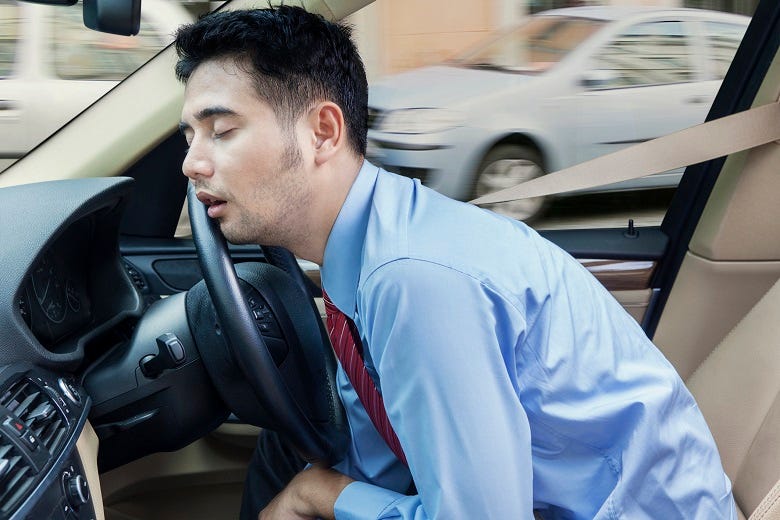 man sleeping behind wheel of car