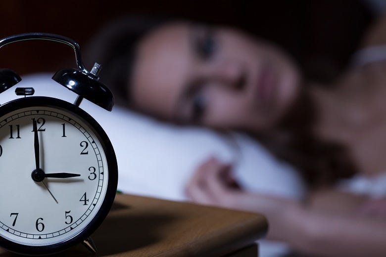 woman in bed staring at alarm clock