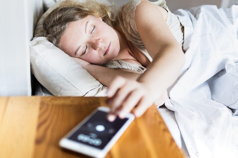 female in bed hitting snooze on her phone