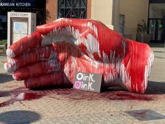 A sculpture is covered in blood, a sign reading "oink oink."