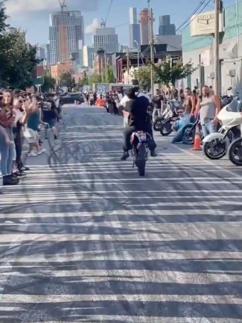 Footage of NYPD Officer Scott on the back of a dirtbike as its operator pops a wheelie.
