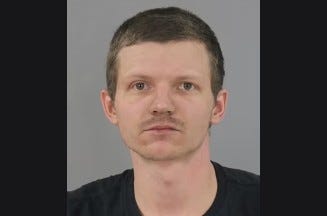 White man with blonde hair and light facial hair wearing a black shirt 