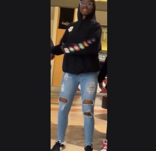 Young Black girl wearing black shoes, torn light blue jeans, black hoodie and clear glasses