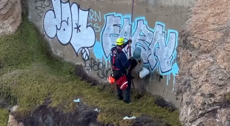 A firefighter rescuing a man who had walked down a San Francisco cliff.
