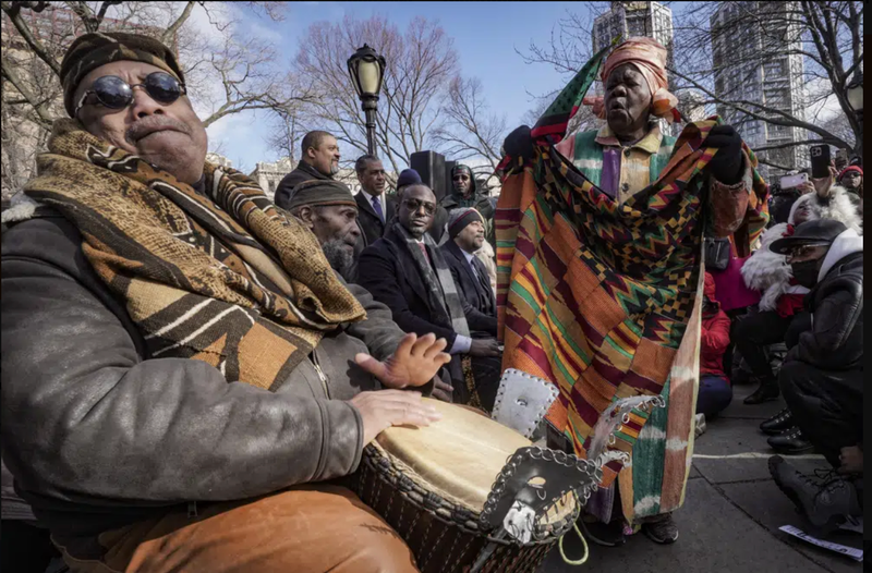 Master drummer Baba Don Babatunde, far left, and civil rights activist Queen Mother Moore, far right, lead a spiritual moment, during the Central Park gate-naming ceremony to honor the five men exonerated after being wrongfully convicted as teenagers for the 1989 rape of a jogger in Central Park, including Yusef Salaam, seated third from left, Raymond Santana Jr., seated fourth from left, Monday Dec. 19, 2022, in New York.