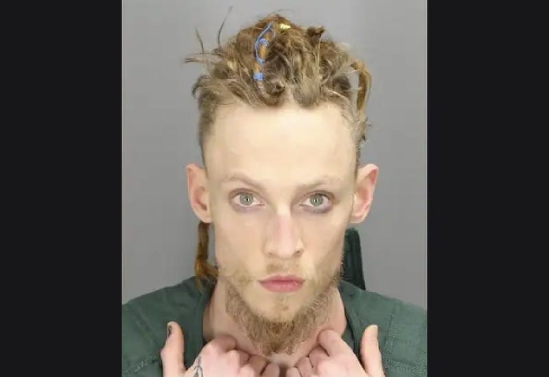 White man in 20s with blond dreads and blonde beard posing for mugshot
