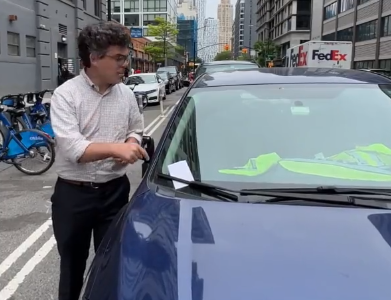 Lincoln Restler announces his new legislation while standing next to a city employee's car using their placard to park in a bike lane.