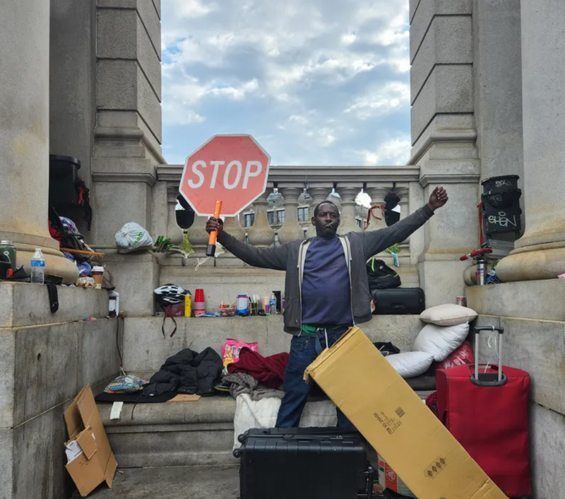 A homeless man defiantly raises a stop sign after police and sanitation workers force him to dismantle his makeshift tarp shelter at the base of the Manhattan bridge on Sept. 22, 2022.