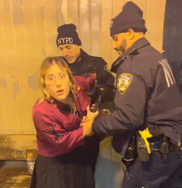 Officers grab the woman who was filming by the wrists before placing her in handcuffs.
