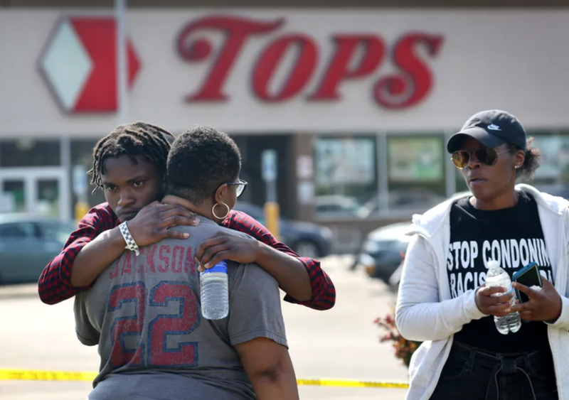 People gathered outside of Tops market embrace on May 15, 2022 in Buffalo, New York. The day before, a gunman opened fire at the store, killing ten people and wounding another three. Suspect Payton Gendron was taken into custody and charged with first degree murder. U.S. Attorney Merrick Garland released a statement, saying the US Department of Justice is investigating the shooting "as a hate crime and an act of racially-motivated violent extremism."