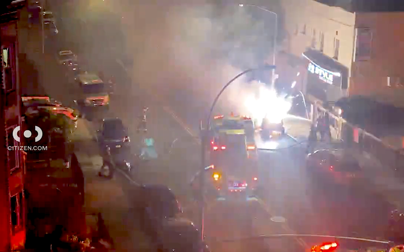 Sparks and flames erupt from a burning vehicle as firefighters respond to the scene