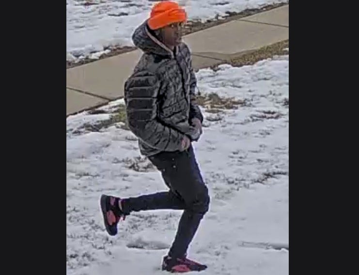 Thin-build man with black pants, orange hat, dark puffer jacket and black and pink shoes