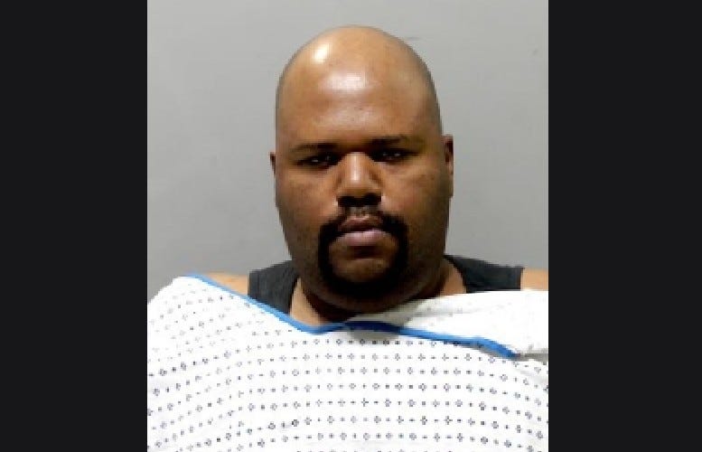 Black man wearing hospital gown with facial hair and bald 