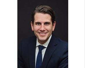 Smiling white man in 40s with slicked back dark hair and wearing a suit