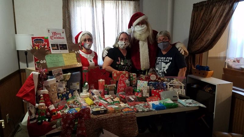 Bonnie, Vicki, Santa, and Patti pose in front of all of the items that go into a Christmas care package