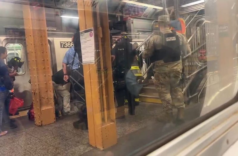 Responders aid a woman who was pushed onto the subway tracks at the Flushing-Main Street station in Queens on Wednesday, and police are looking for the culprit.