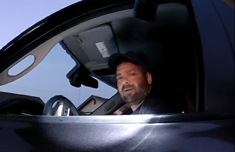 Suspect seen through the driver-side window of his truck. Wearing a dark baseball cap.