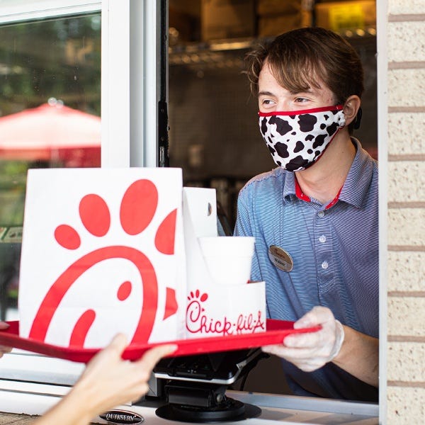 A Chick-fil-A employee hands a customer their order through a takeout window.