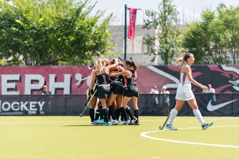 The Saint Joseph’s University field hockey team celebrates on the field.