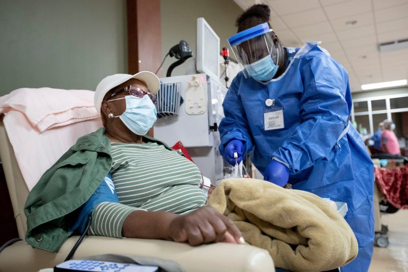 A patient sits in a chair as a technician connects her to a dialysis machine.