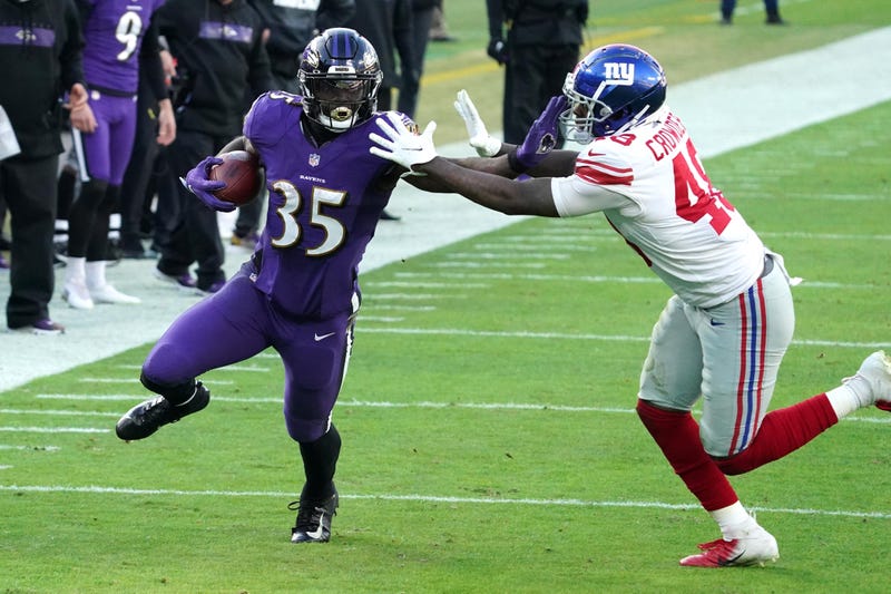 Ravens RB Gus Edwards stiff arms a defender