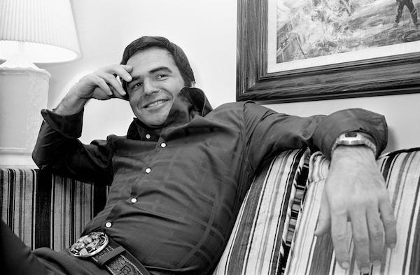 Burt Reynolds smiling on couch
