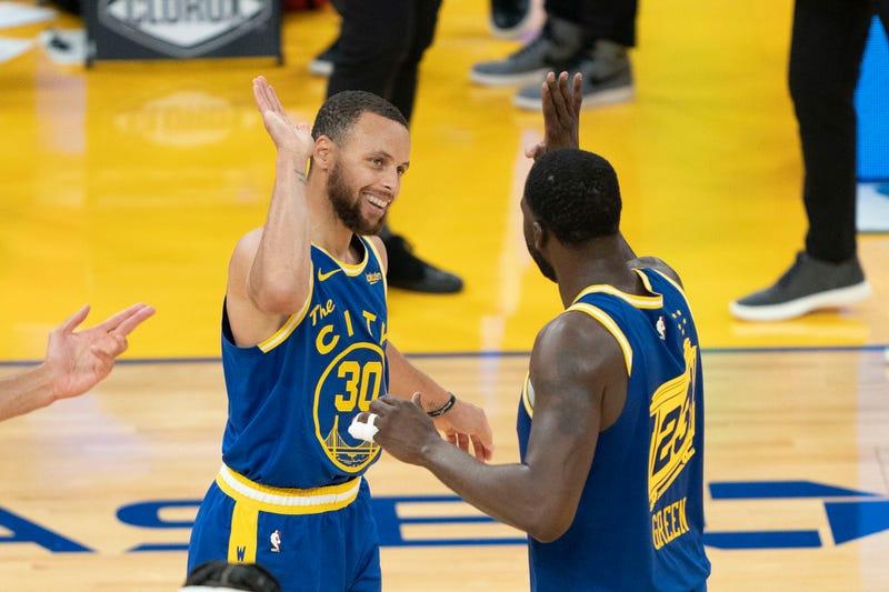 Warriors stars Steph Curry and Draymond Green high-five on the court.